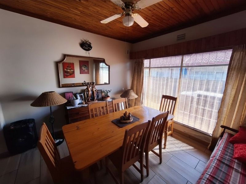 A dining room featuring a timber ceiling, ceiling fan, and tiled flooring, with large windows providing natural light.