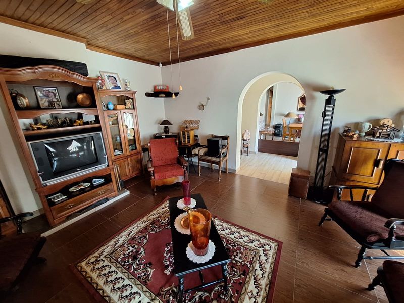 A living room featuring a timber ceiling, tiled flooring, and an arched doorway leading to an adjacent dining area.