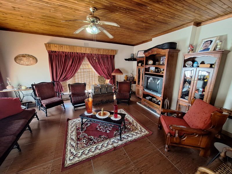 A spacious living room featuring a warm timber-clad ceiling, ceiling fan, and tiled flooring, complemented by built-in wooden cabinetry.