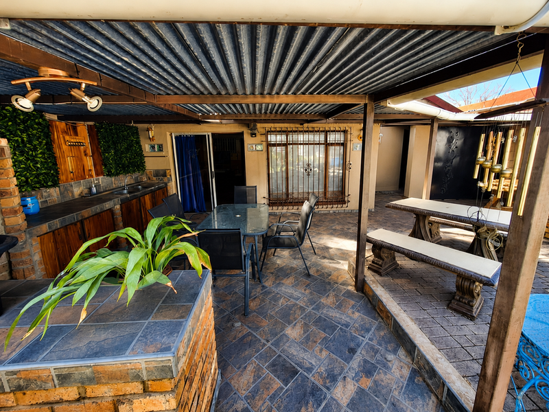 Covered outdoor patio area featuring a built-in brick braai, tiled prep surfaces, sink, and paved flooring, ideal for alfresco dining and entertainment.