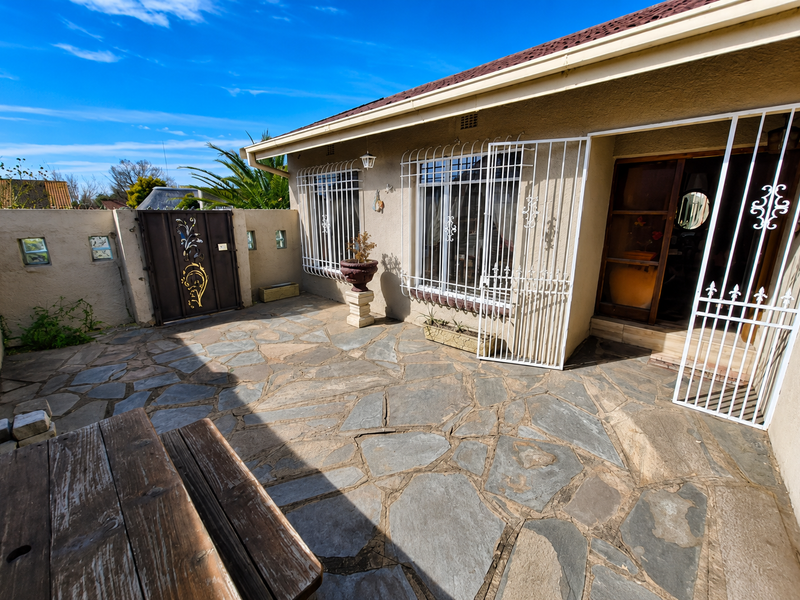 A paved outdoor patio area featuring security gates and bars, enclosed by a boundary wall, offering a functional space for outdoor living.