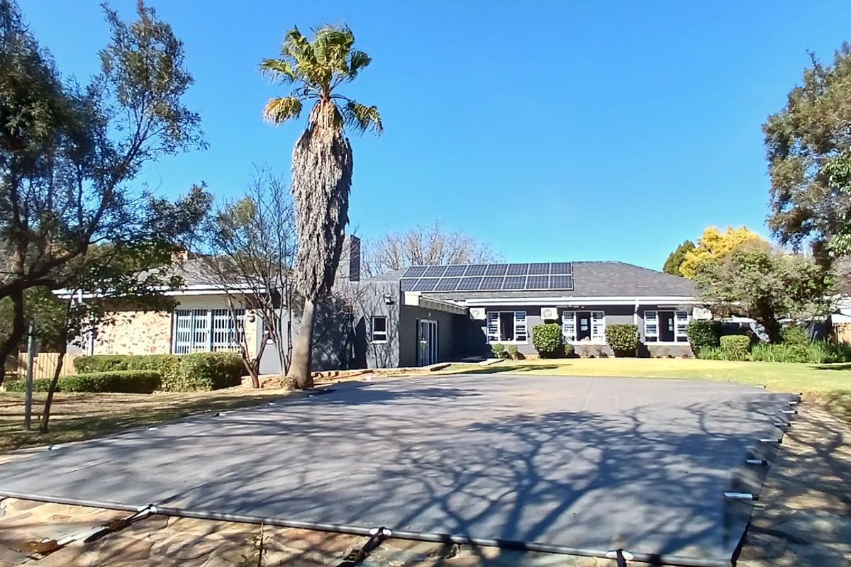 Rear view of the property featuring a swimming pool with a cover, solar panels on the roof, and a spacious landscaped garden.