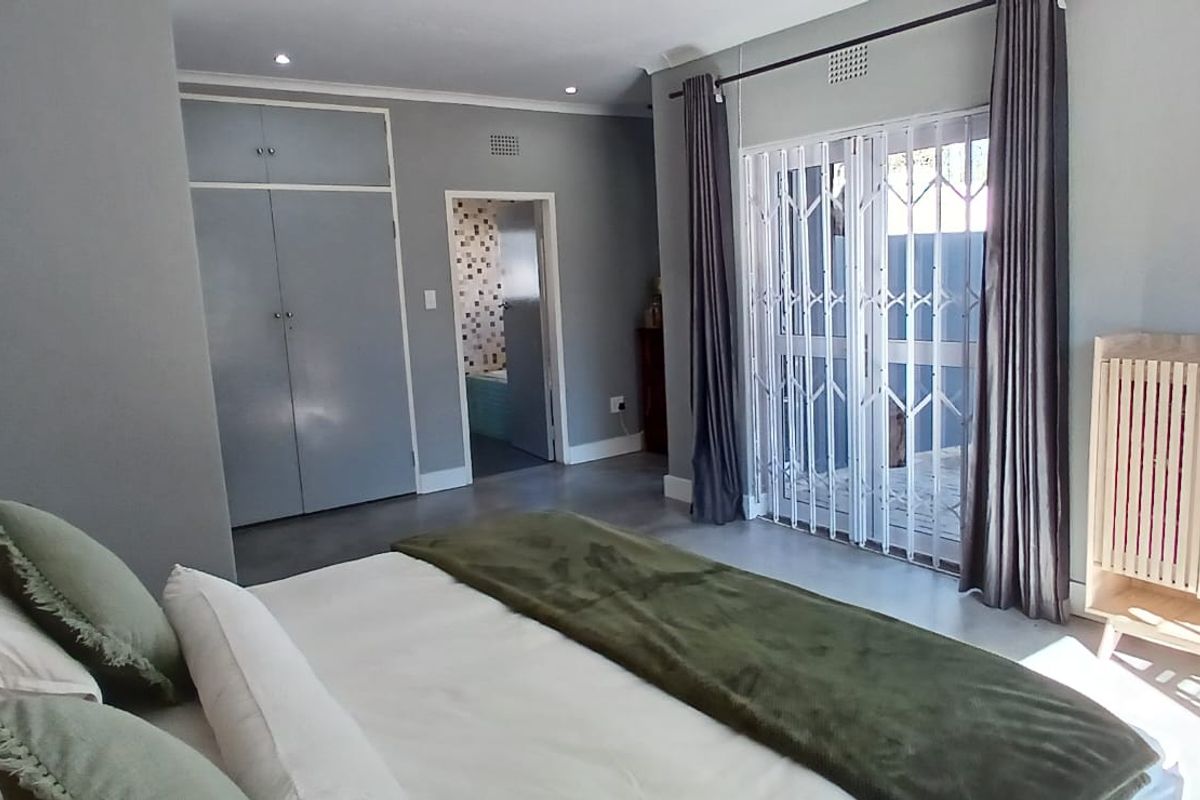 A well-maintained bedroom featuring built-in cupboards, recessed lighting, and a sliding door with a security gate leading to the exterior.