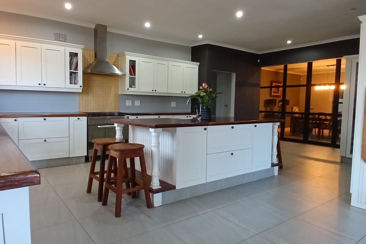 A well-appointed kitchen featuring a central island with wooden countertops, white cabinetry, stainless steel extractor fan, and modern tiled flooring.