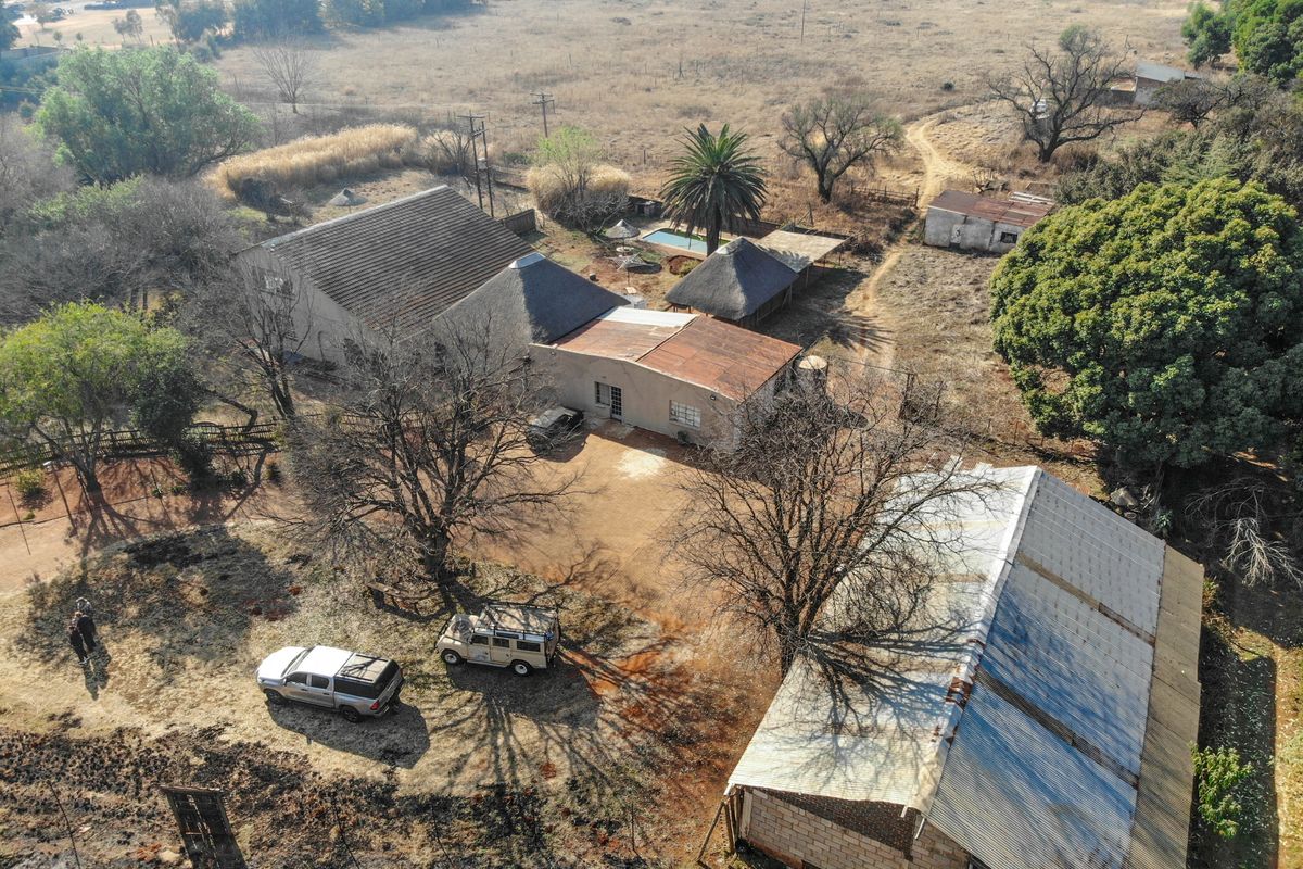 Aerial view of a rural property featuring multiple structures, including a main house with thatched and tiled roofing, a swimming pool, and an outbuilding.