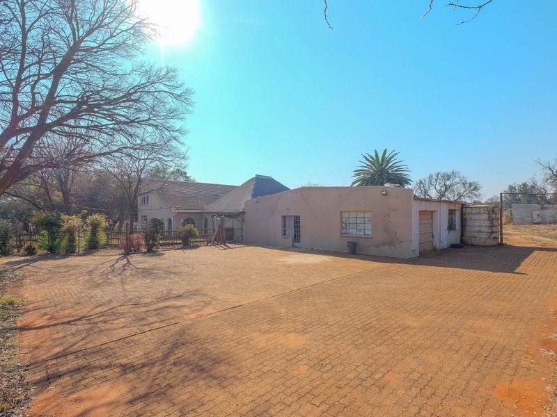 Spacious paved driveway leading to a garage and main house structure, featuring a water tank and established garden surroundings.