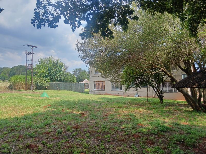 A view of the rear garden and property exterior, featuring a lawn, mature trees, and a small thatched outdoor structure.