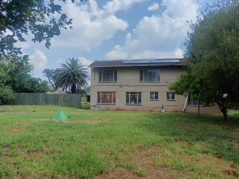 Rear view of a two-story residential property featuring a large garden, solar panels on the roof, and security bars on the windows.