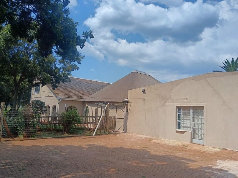 Rear exterior view of the property featuring a combination of thatched and tiled roofing, paved driveway area, and perimeter security fencing.