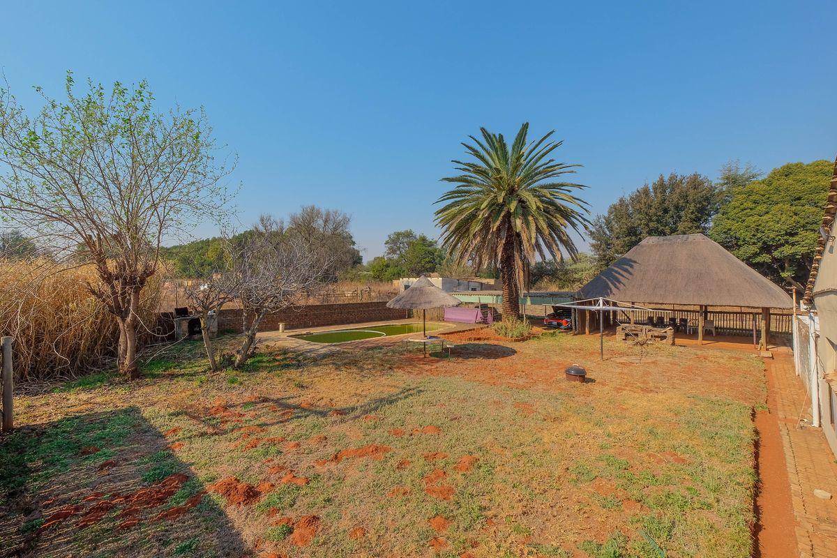 Spacious rear garden featuring a swimming pool, a traditional thatch roof lapa, and established trees, offering significant potential for outdoor landscaping and entertainment area upgrades.