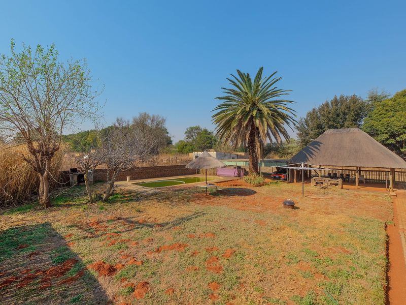 Spacious rear garden featuring a swimming pool, a traditional thatch roof lapa, and established trees, offering significant potential for outdoor landscaping and entertainment area upgrades.