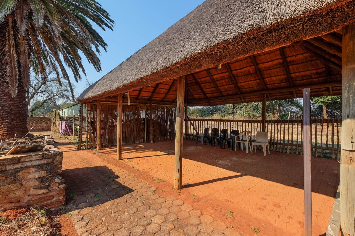 An open-air thatched lapa area featuring timber support posts and paved flooring, providing a rustic outdoor entertainment space.