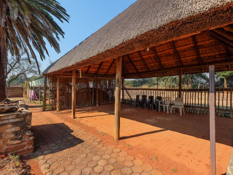 An open-air thatched lapa area featuring timber support posts and paved flooring, providing a rustic outdoor entertainment space.