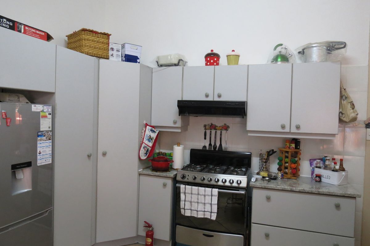 A functional kitchen featuring light grey cabinetry, stone countertops, a gas stove with an extractor fan, and tiled flooring.