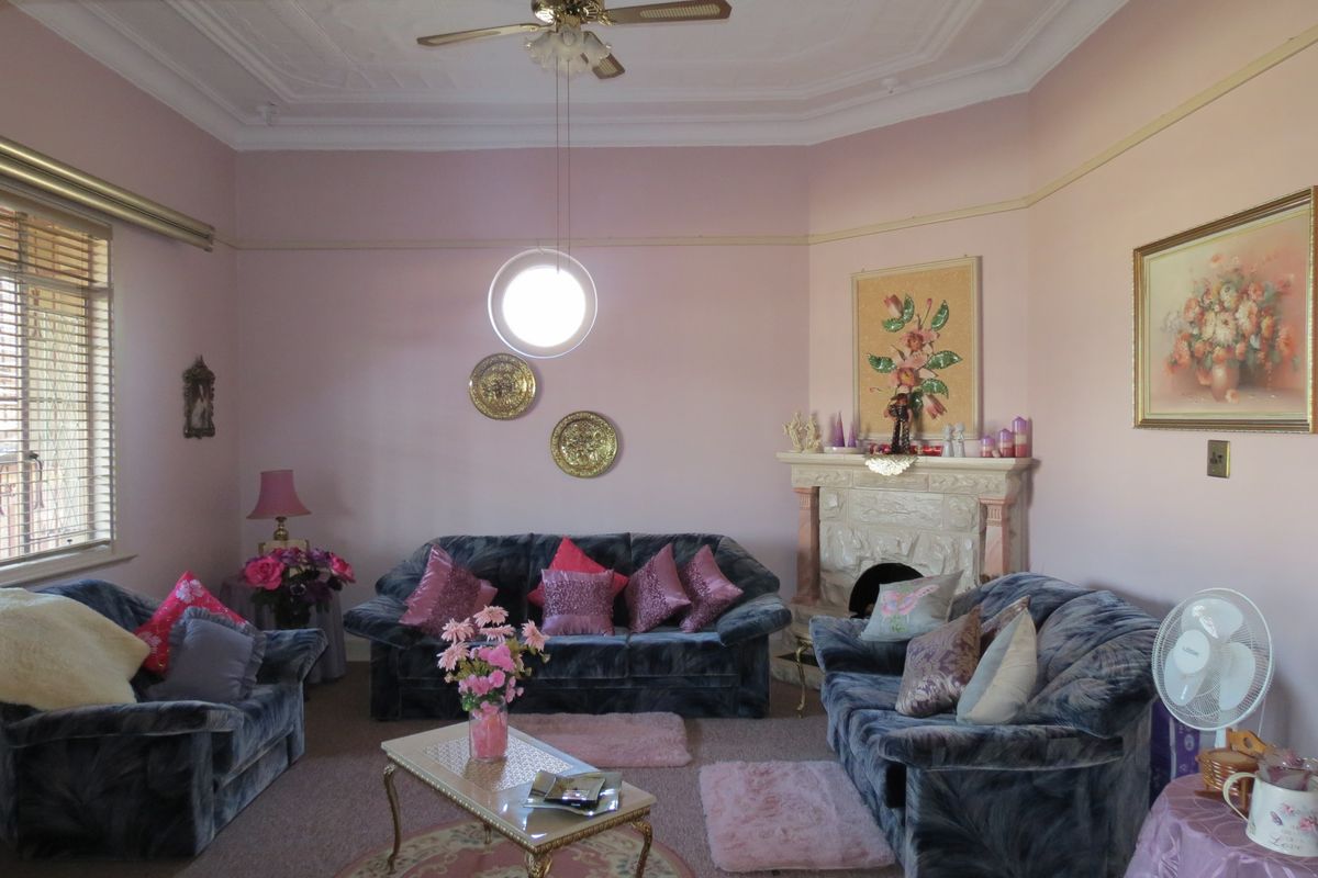 A traditional living room featuring an ornate ceiling rose, a ceiling fan, and a stone fireplace, offering a classic architectural foundation.