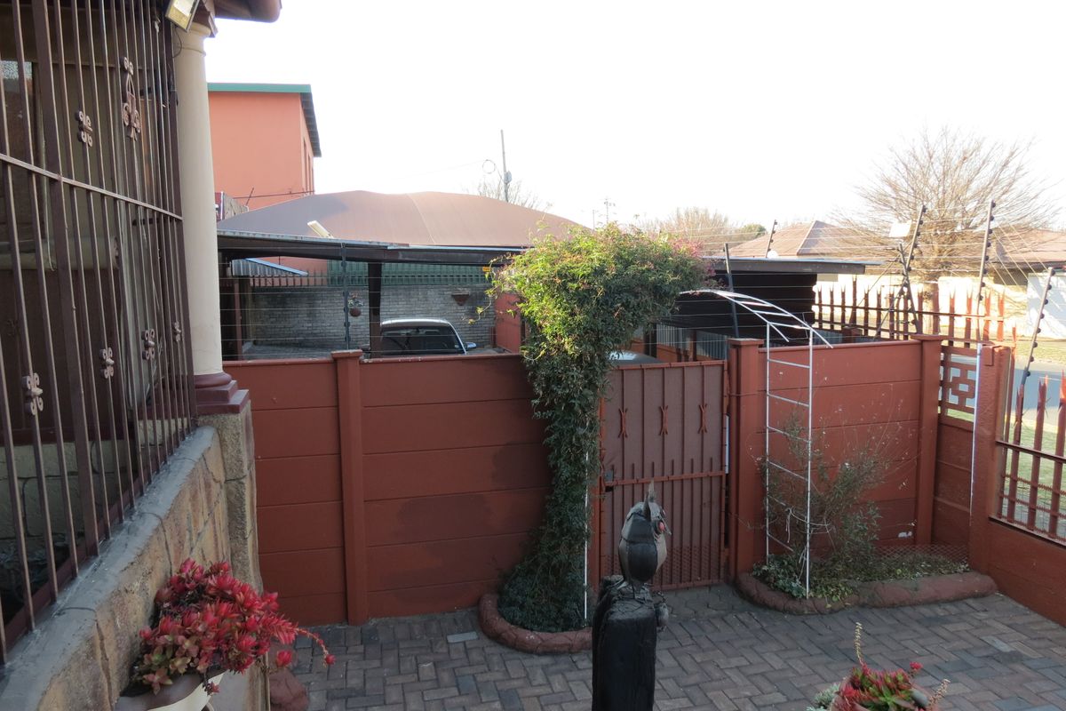 Rear courtyard area featuring paved flooring, a metal security gate, and a carport structure enclosed by a precast concrete boundary wall with electric fencing.