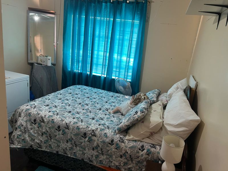 A bedroom featuring a window with curtains and visible wall surface wear, requiring cosmetic updates to improve the overall condition.