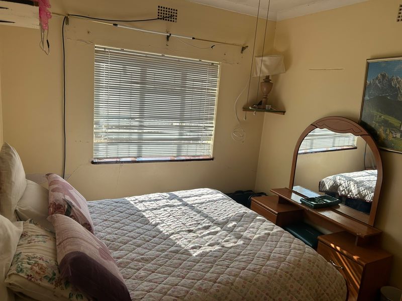 A bedroom featuring a window with venetian blinds and a ceiling vent, currently showing significant signs of wall damage and wear.
