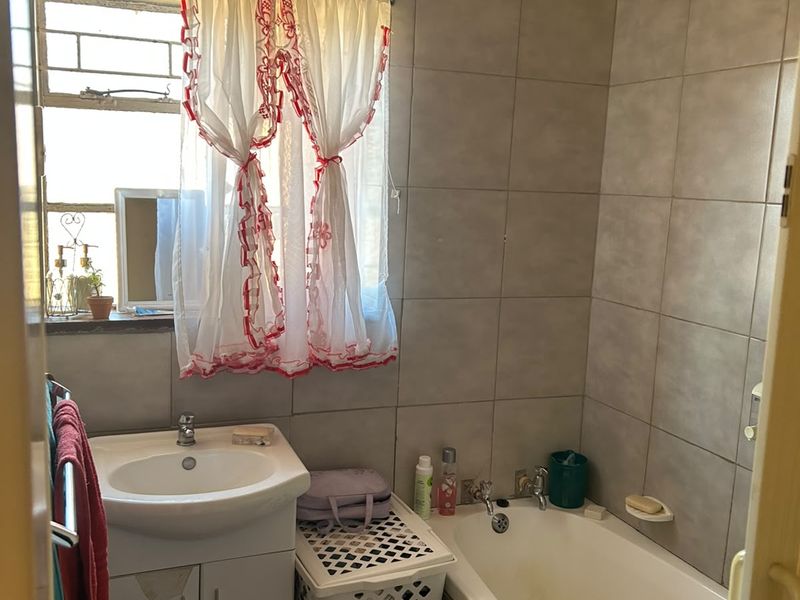 A compact bathroom featuring a built-in vanity, bathtub, and full-height wall tiling. The space would benefit from modern updates to fixtures and finishes.
