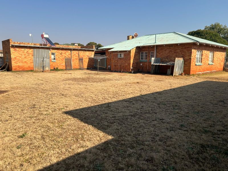 Rear view of a brick house featuring a corrugated metal roof, solar water heating system, and a large open backyard area.