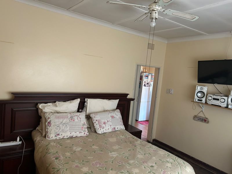 A bedroom featuring a ceiling fan and coved cornicing, requiring cosmetic updates to the wall finishes and flooring to improve its overall condition.