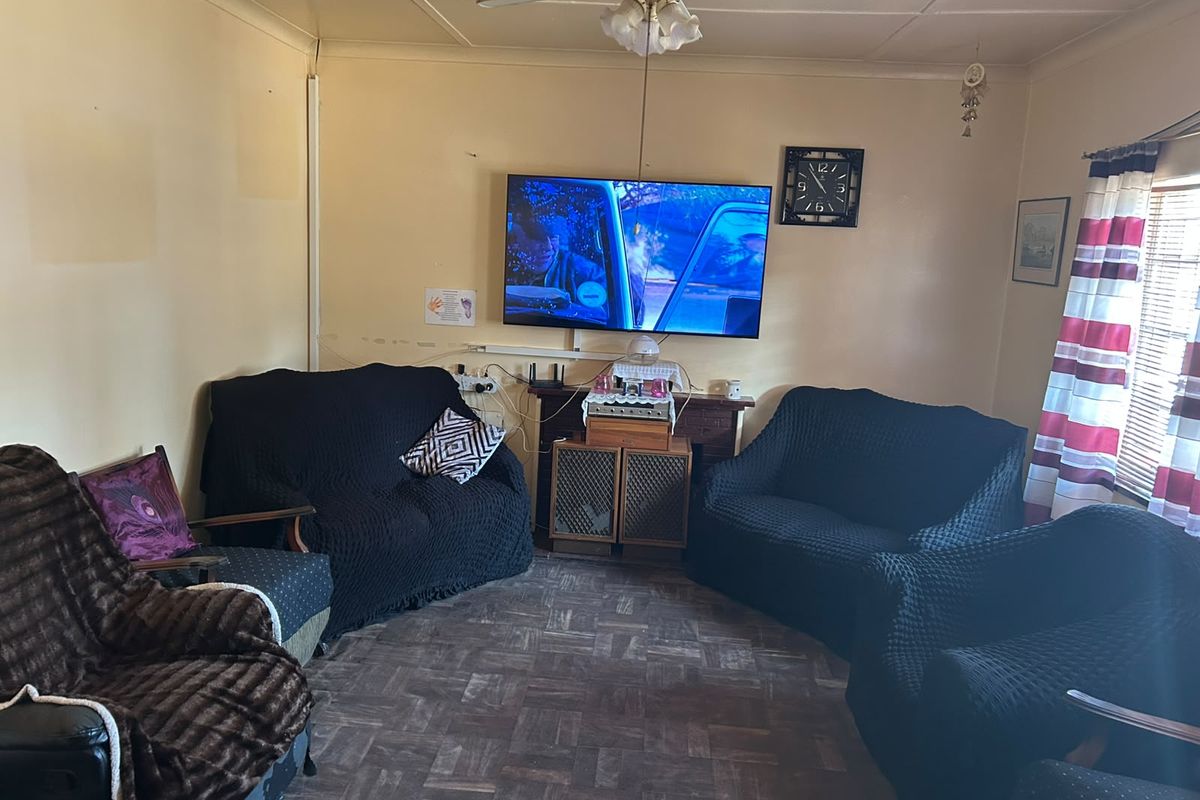 A living room featuring parquet flooring and a ceiling fan, currently showing signs of wear on the wall surfaces.