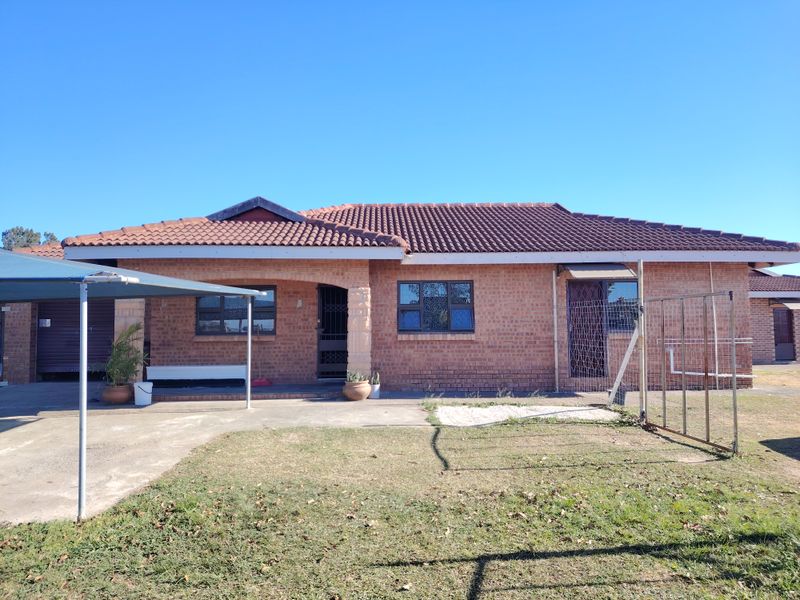 Rear view of a single-story face brick house featuring a tiled roof, concrete patio area, and metal carport structure.