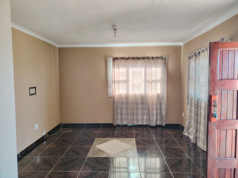 An empty living room featuring dark patterned tiled flooring, neutral wall paint, and a solid timber entrance door.