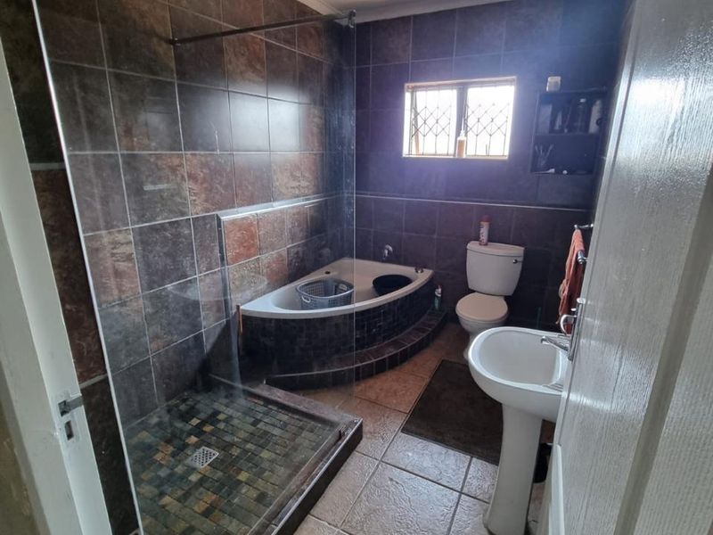 A functional bathroom featuring a walk-in shower with glass screen, corner bathtub, pedestal basin, and toilet, finished with dark tiled walls and flooring.