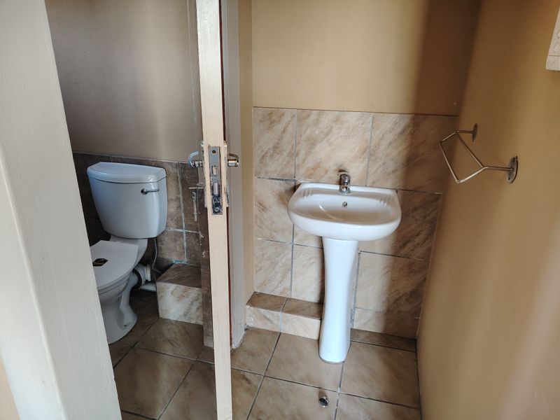 A compact bathroom featuring a pedestal basin, toilet, and tiled finishes, presenting a functional space ready for cosmetic updates.