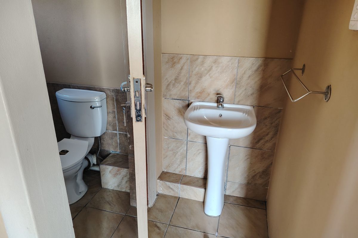A compact bathroom featuring a pedestal basin, toilet, and tiled finishes, presenting a functional space ready for cosmetic updates.