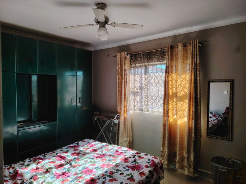 A bedroom featuring built-in cupboards, a ceiling fan, and a window fitted with a security gate.