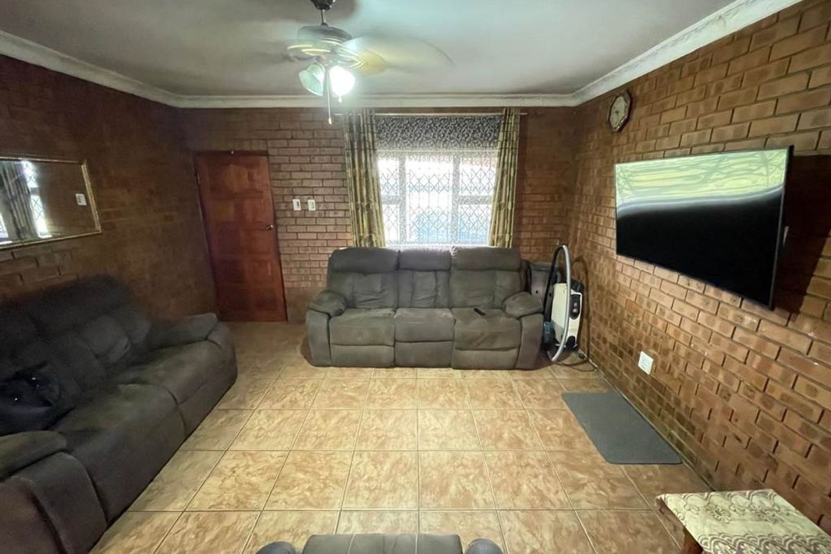 A living room featuring exposed brick walls, ceramic floor tiles, and a ceiling fan, offering a rustic aesthetic with potential for modern updates.