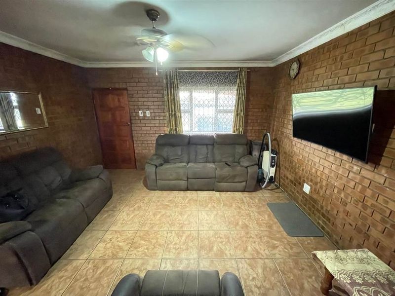A living room featuring exposed brick walls, ceramic floor tiles, and a ceiling fan, offering a rustic aesthetic with potential for modern updates.