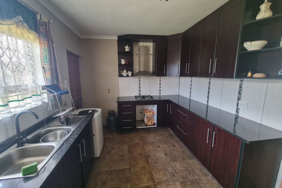 A functional kitchen featuring dark wood cabinetry, granite countertops, a gas hob with extractor fan, and tiled flooring.