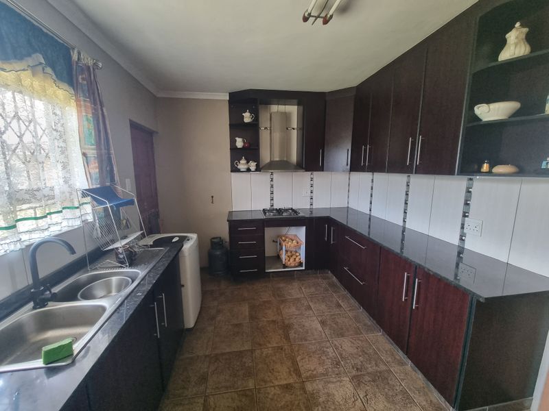 A functional kitchen featuring dark wood cabinetry, granite countertops, a gas hob with extractor fan, and tiled flooring.