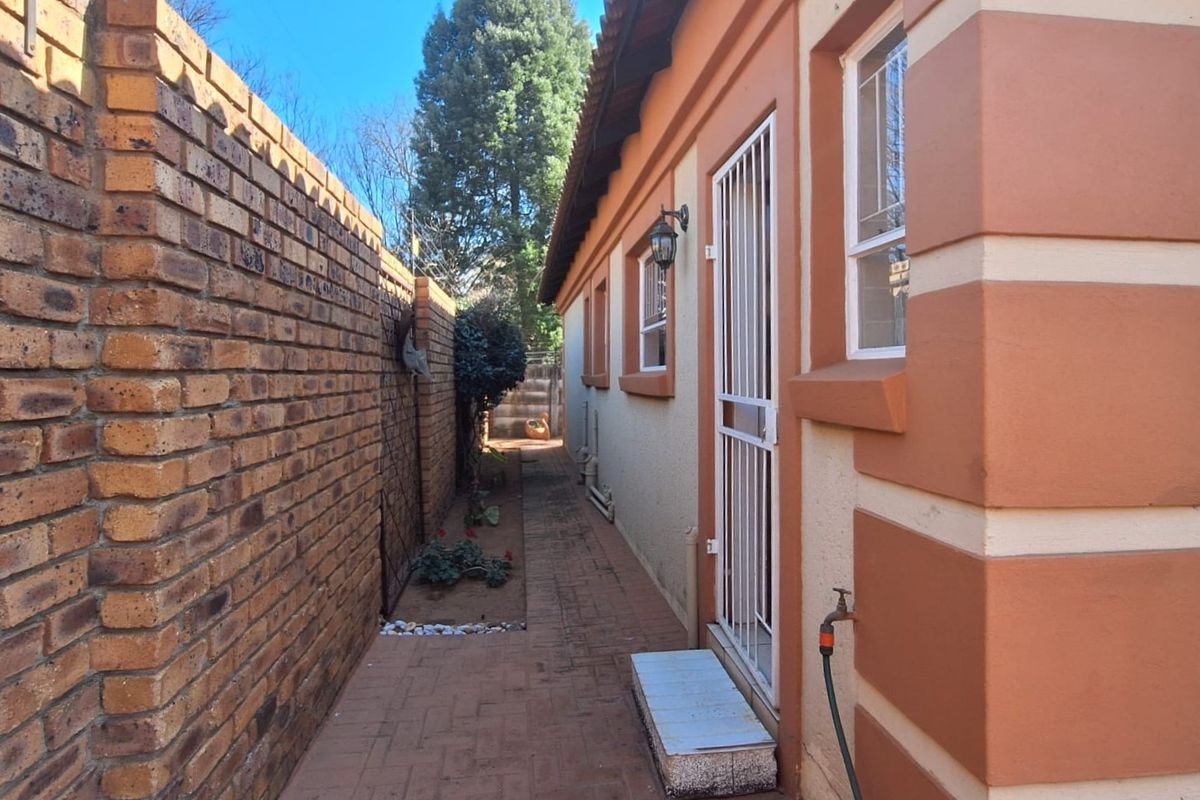 A side exterior view of the townhouse featuring a paved walkway, brick boundary wall, and a secure entrance door.