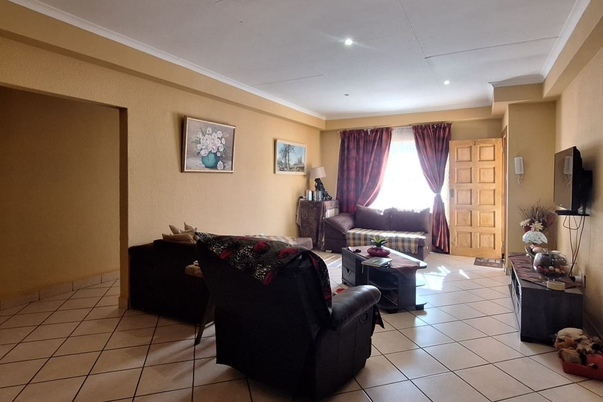 A spacious living room featuring tiled flooring, recessed downlighting, and a timber panelled entrance door, offering a comfortable and functional living space.