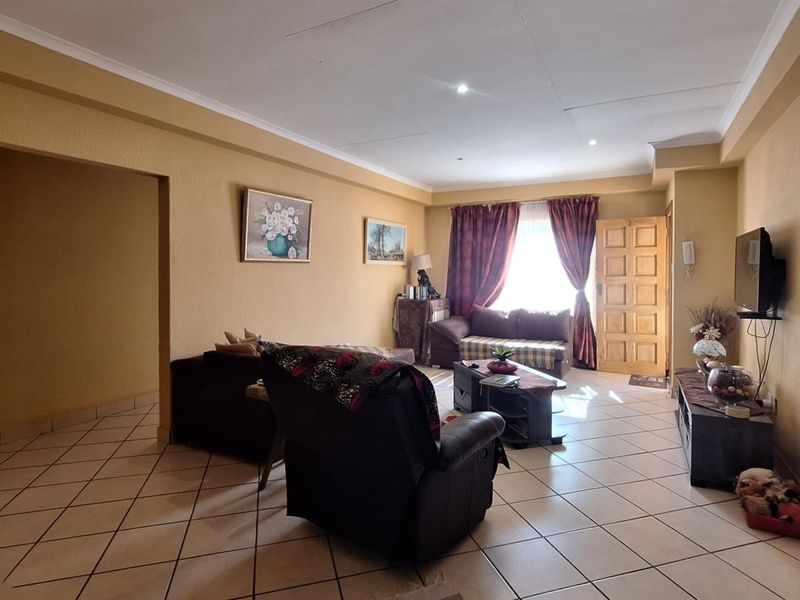 A spacious living room featuring tiled flooring, recessed downlighting, and a timber panelled entrance door, offering a comfortable and functional living space.