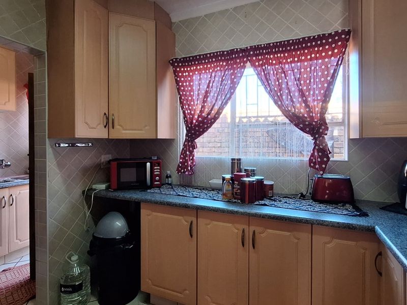 A functional kitchen featuring laminate cabinetry, tiled backsplash, and tiled flooring, with an adjacent scullery area visible through the doorway.