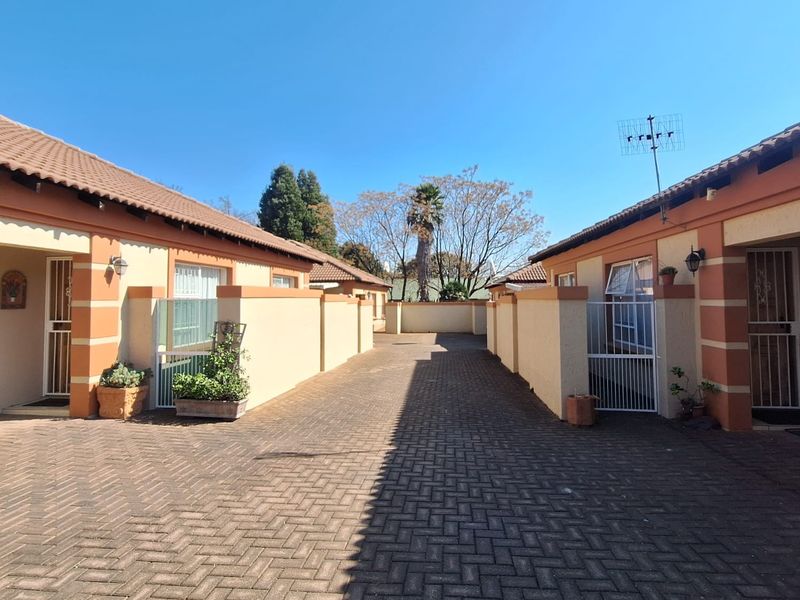 A view of the paved driveway and entrance area between two townhouse units, featuring security gates and well-maintained exterior walls.