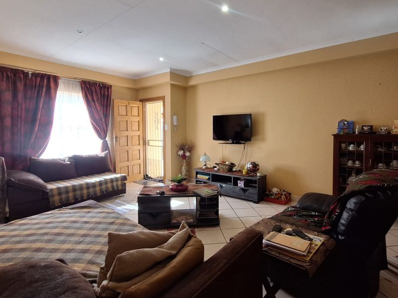 A spacious living room featuring tiled flooring, recessed ceiling lights, and direct access to the exterior via a secure timber panel door.