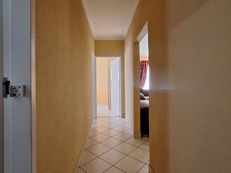 A clean, functional hallway featuring neutral textured walls and diamond-patterned ceramic floor tiles, providing access to adjacent rooms.