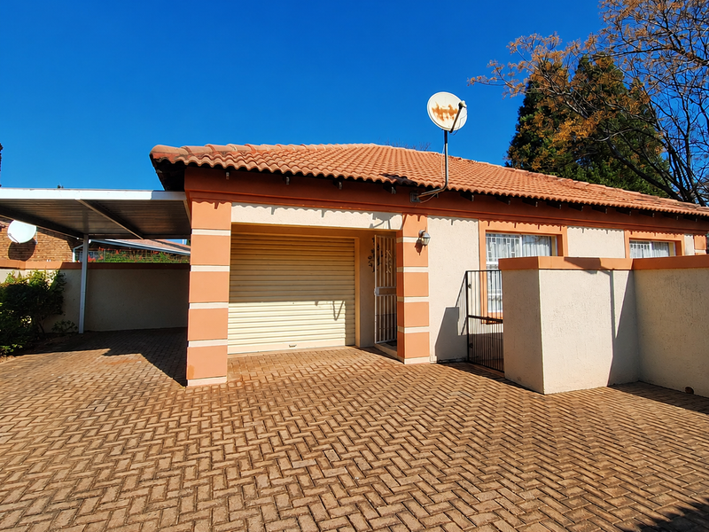 Front exterior view of a townhouse featuring a paved driveway, integrated garage with roller door, carport, and secure boundary walling.