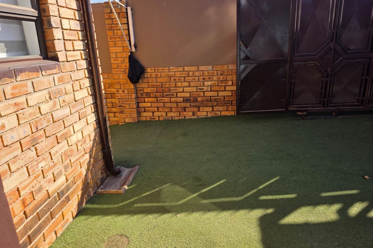 A compact rear courtyard area featuring face brick walls, artificial grass surfacing, and a secure metal gate.