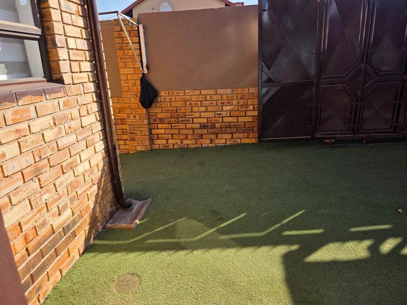 A compact rear courtyard area featuring face brick walls, artificial grass surfacing, and a secure metal gate.
