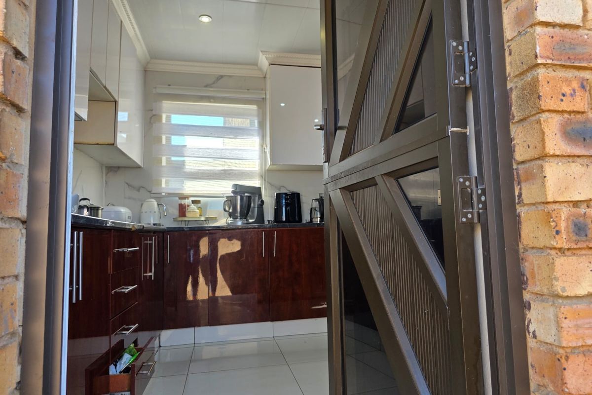 A view into a kitchen featuring glossy cabinetry, stone countertops, and tiled flooring, accessed through an aluminium framed door.