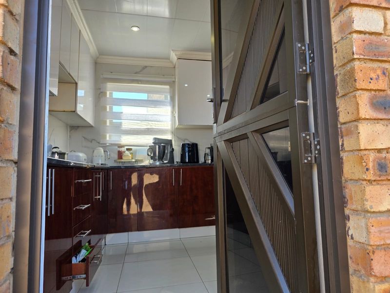 A view into a kitchen featuring glossy cabinetry, stone countertops, and tiled flooring, accessed through an aluminium framed door.