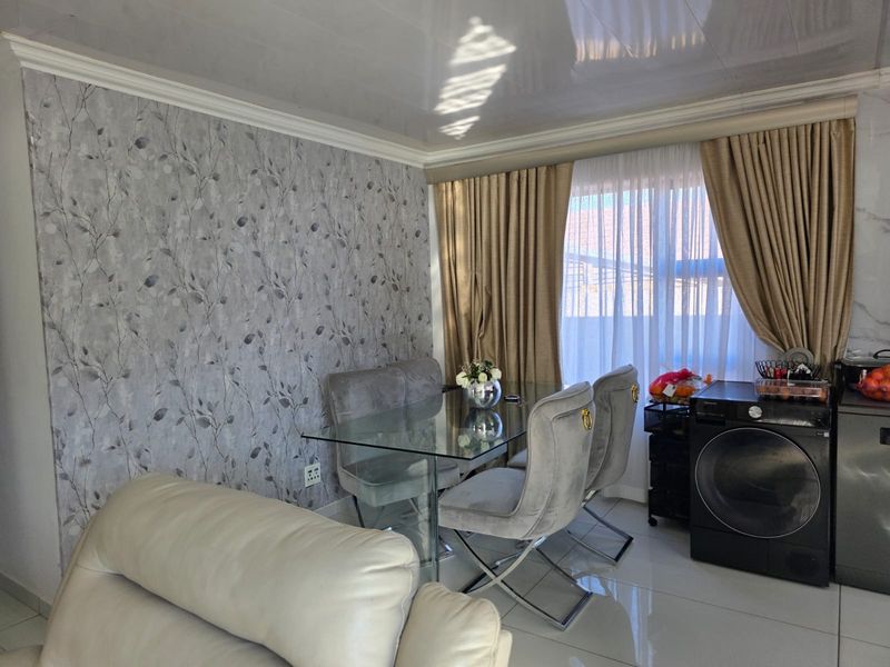 A living area featuring glossy floor tiles, coved ceiling detailing, and a decorative patterned feature wall.