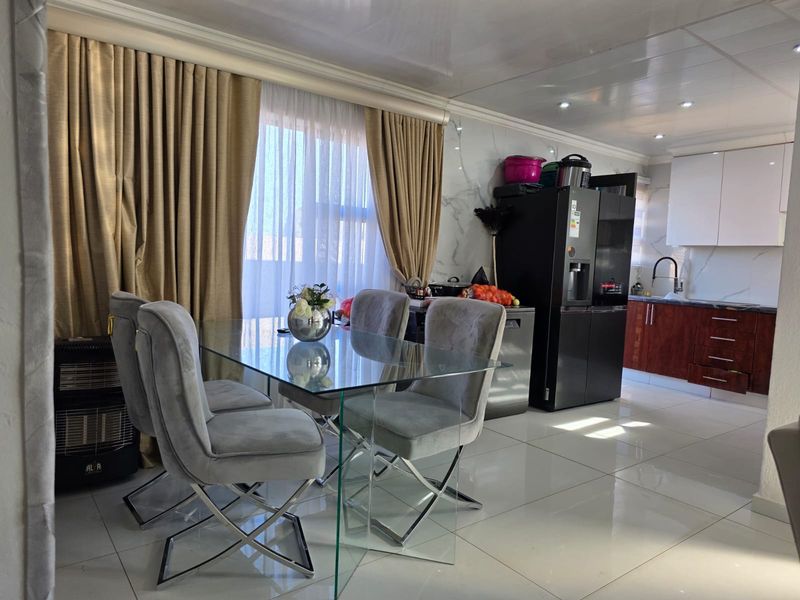 Modern open-plan living and dining area featuring glossy floor tiles, marble-effect wall finishes, and a contemporary kitchen with sleek cabinetry.